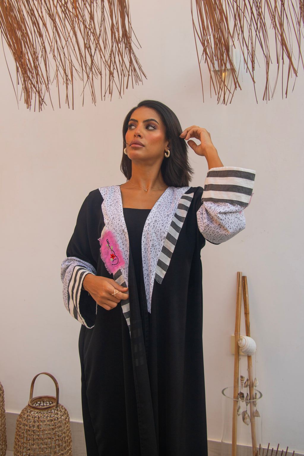 Close-up of PEONISA Raneem black abaya showing striped sleeve cuffs, light patterned front trim and pink detail.